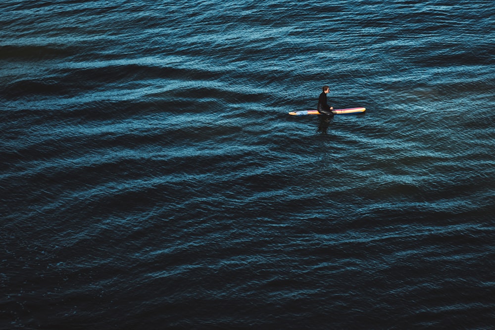 personne en combinaison noire surfant sur l’eau de mer bleue pendant la journée