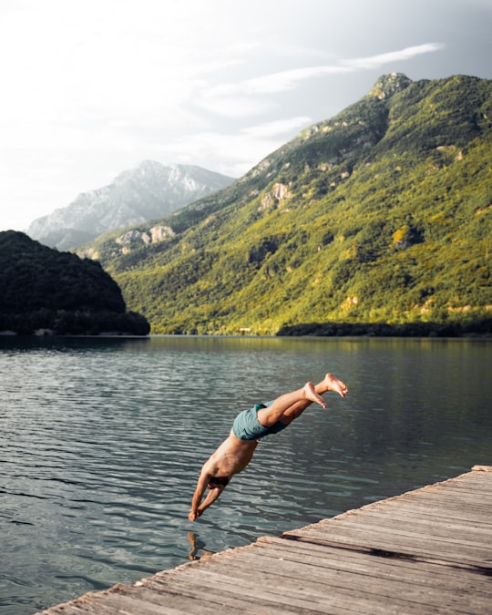 woman in teal bikini jumping on water near green mountain during daytime in Comune di Cavazzo Carnico Italy