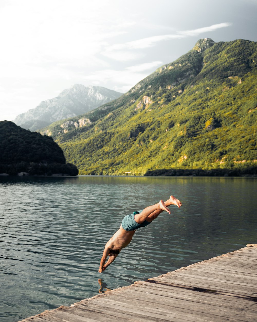 woman in teal bikini jumping on water near green mountain during daytime