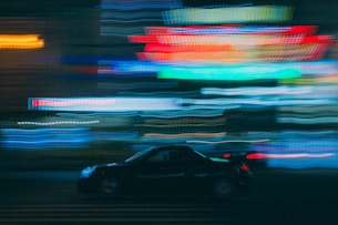 A dynamic shot of a luxury car speeding through a dark city street lit by yellow neon signs.