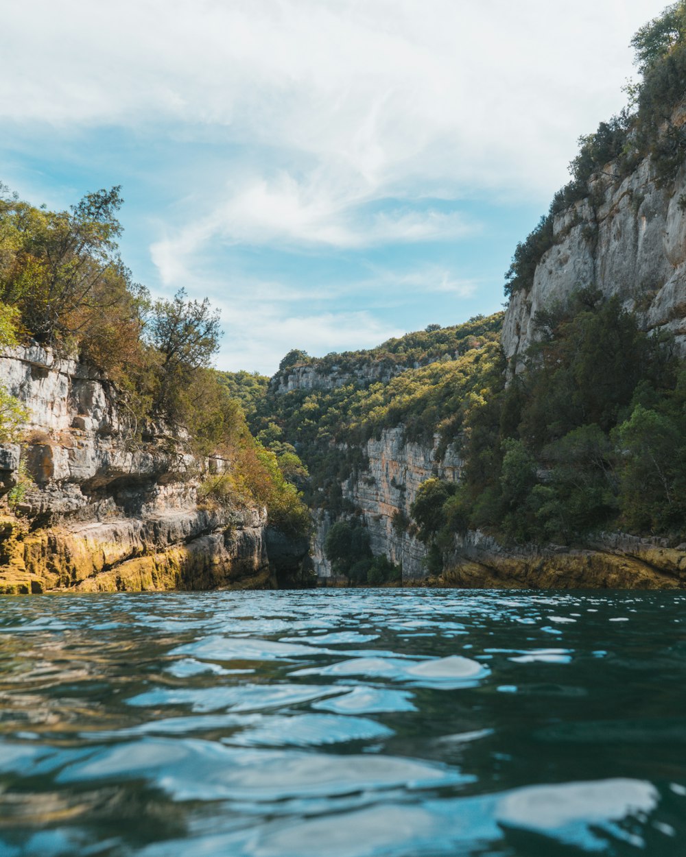 montaña rocosa verde y marrón al lado del cuerpo de agua bajo cielo nublado azul y blanco durante