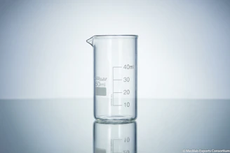 Close-up of a skilled technician inspecting a clear borosilicate glass beaker in a bright laboratory.