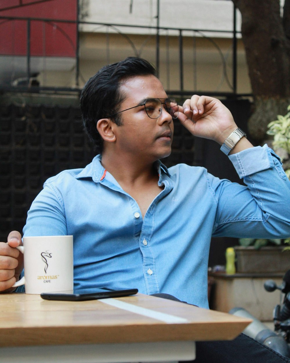 man in blue dress shirt holding white ceramic mug