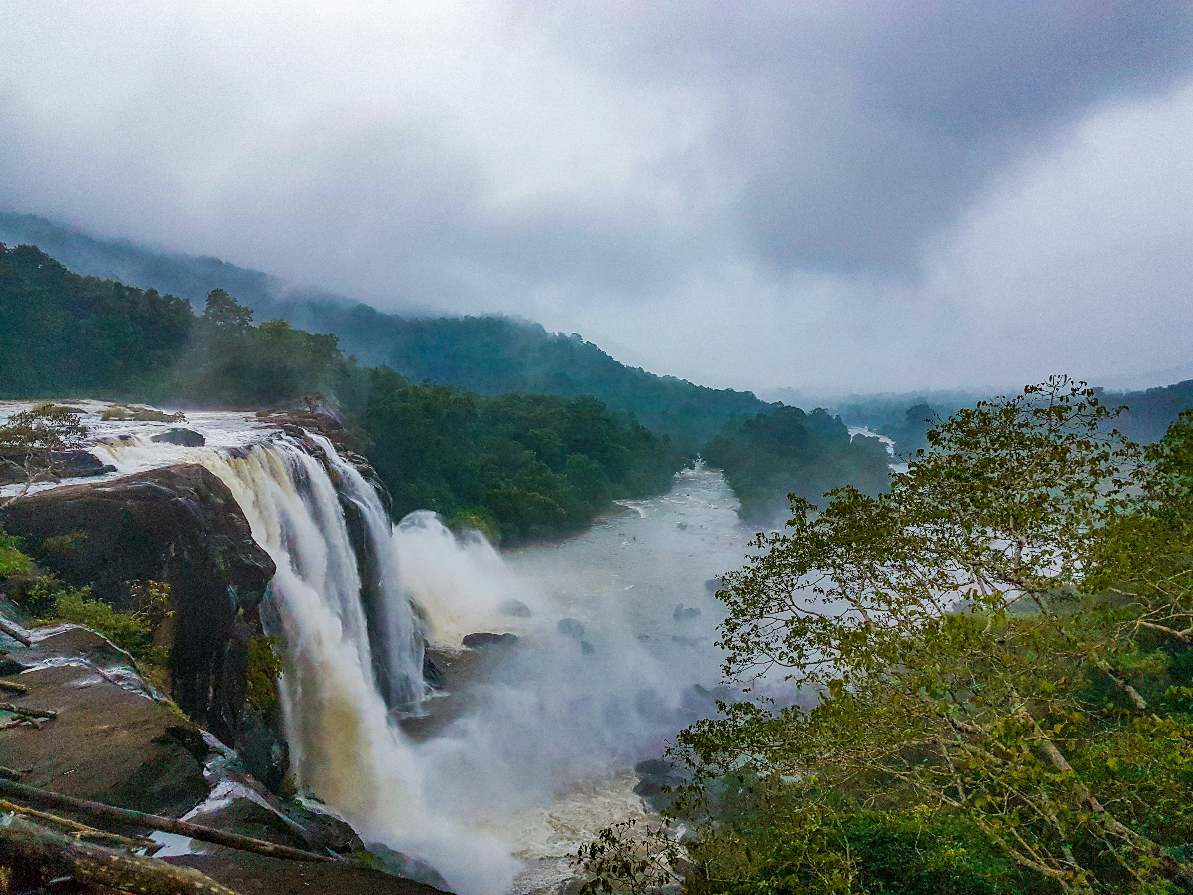 waterfalls near green trees under white sky during daytime