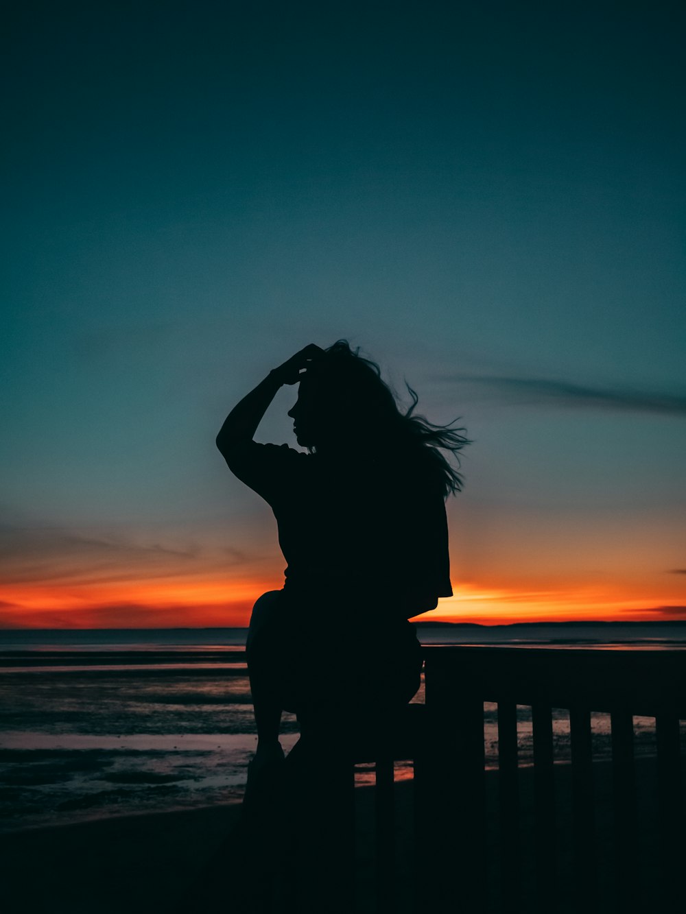 Silhouette einer Frau, die während des Sonnenuntergangs am Strand steht