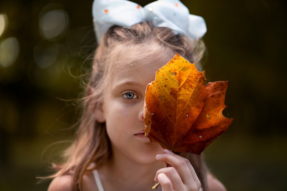 girl in white tank top holding brown leaf