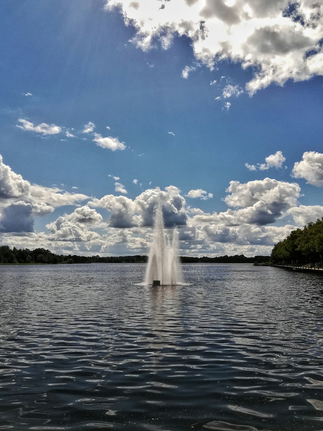 water fountain on body of water under blue sky and white clouds during daytime