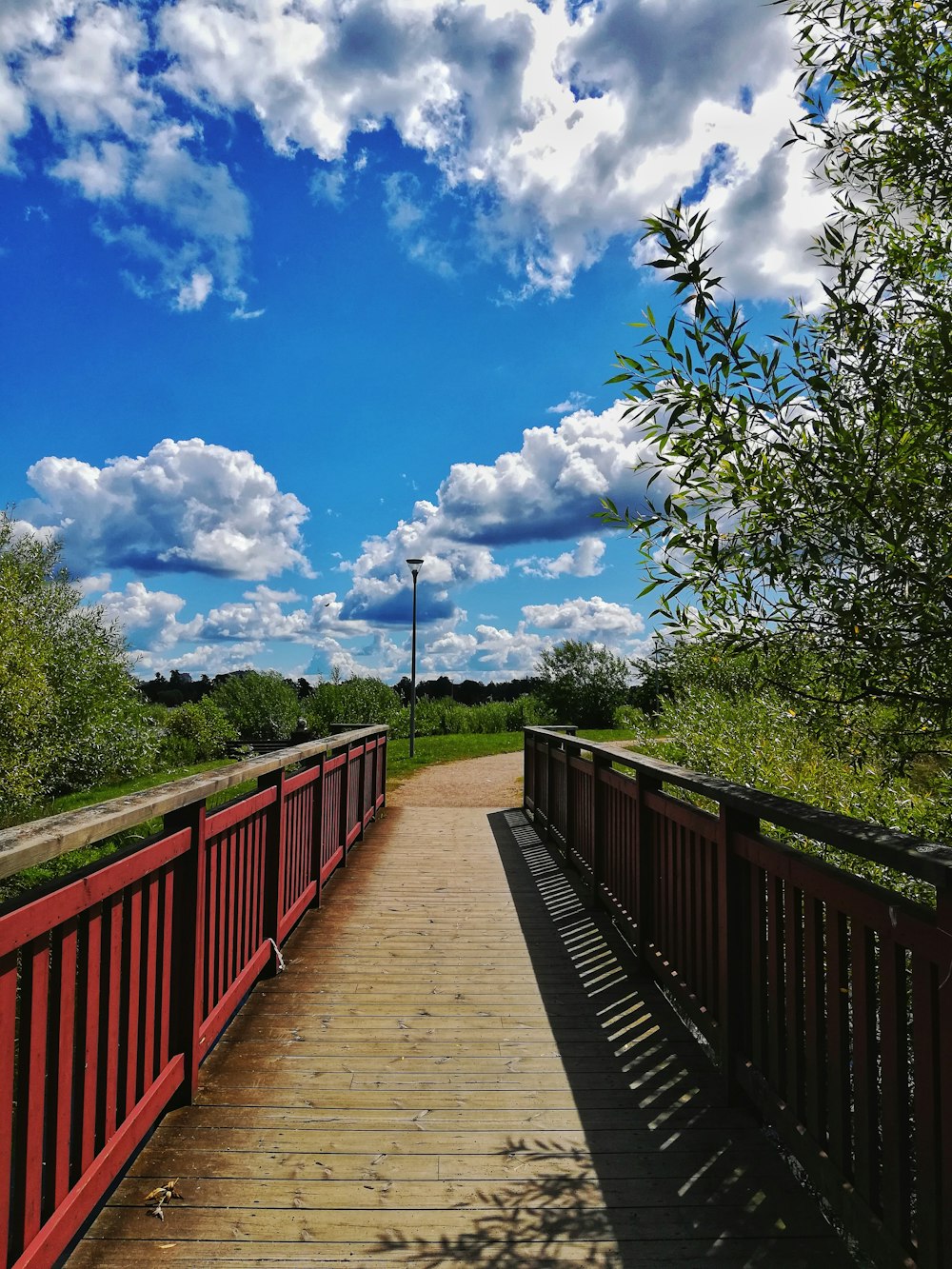 Puente de madera marrón sobre campo de hierba verde bajo cielo azul y nubes blancas durante el día
