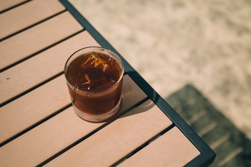 clear drinking glass with brown liquid on white wooden table