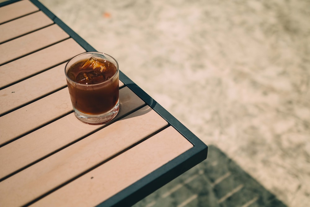 clear drinking glass with brown liquid on brown wooden table