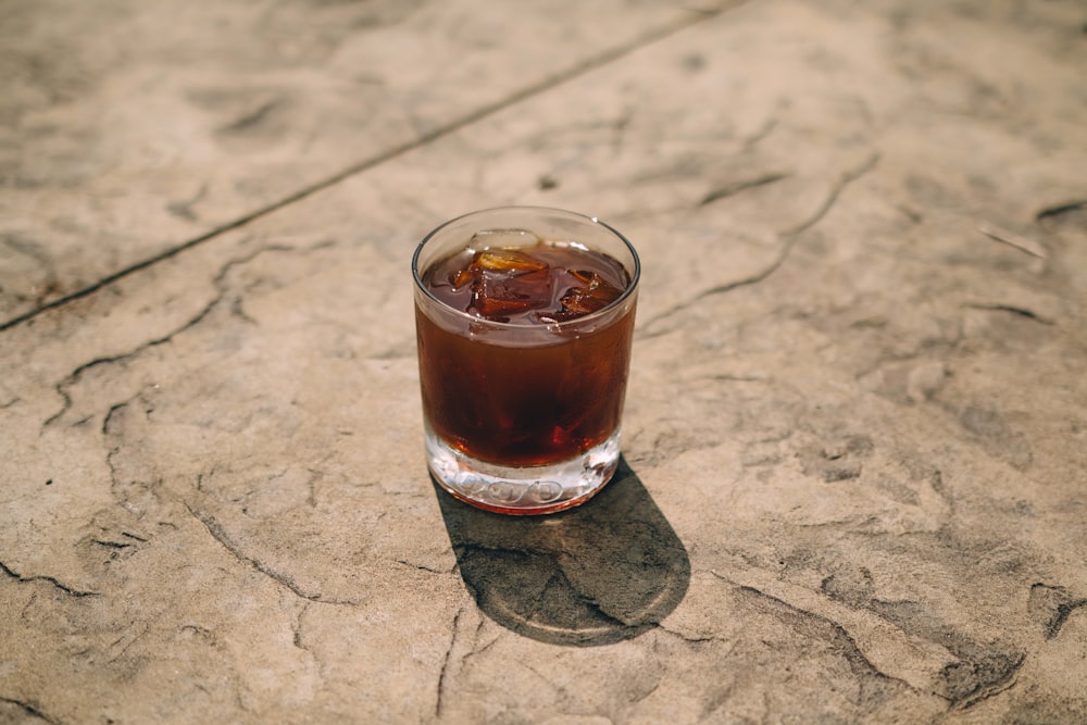 clear drinking glass with brown liquid on brown wooden table