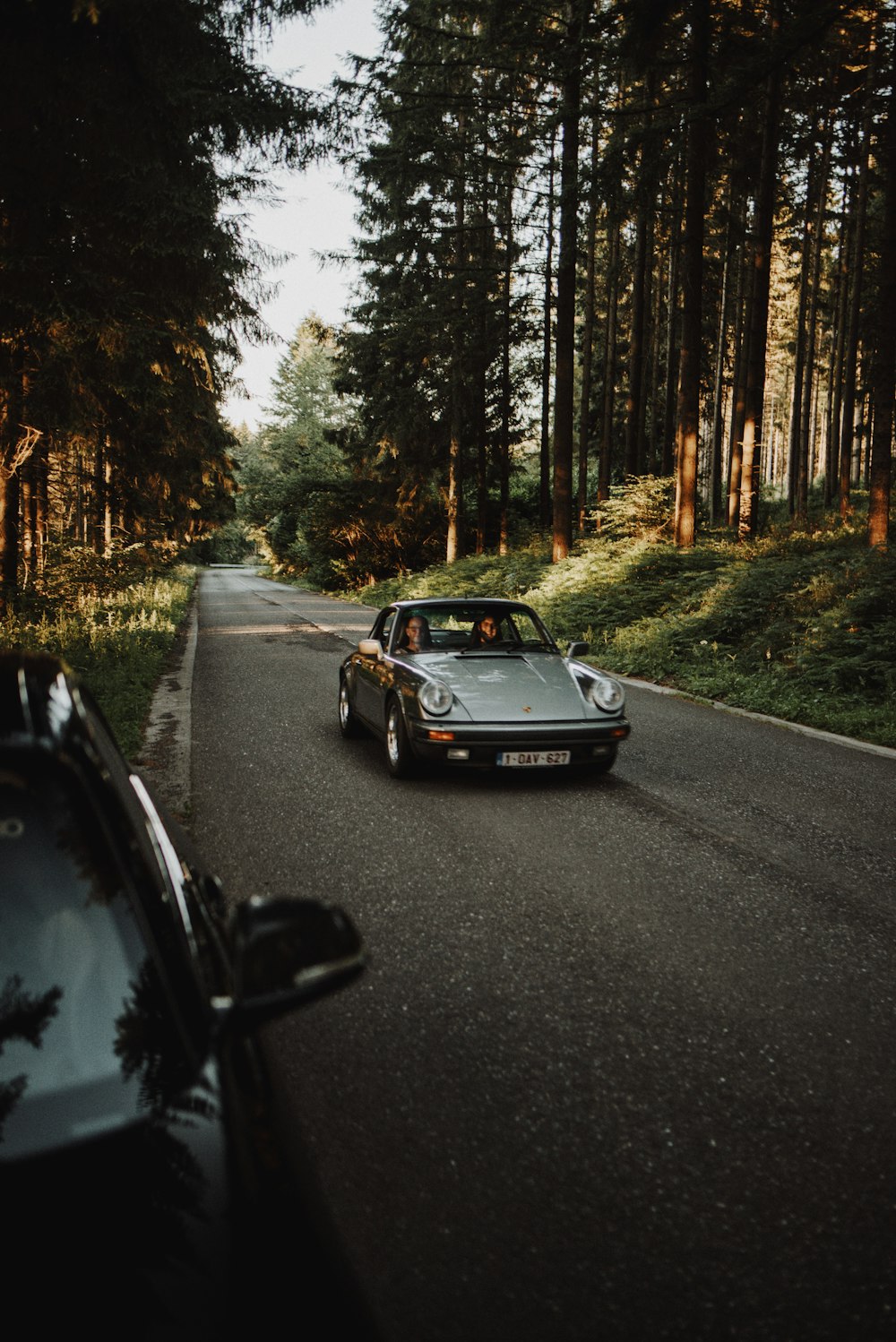 Porsche 911 negro en la carretera entre árboles durante el día