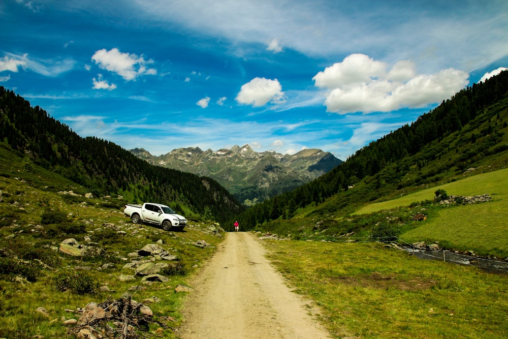 white car on road near green grass field and mountains during daytime