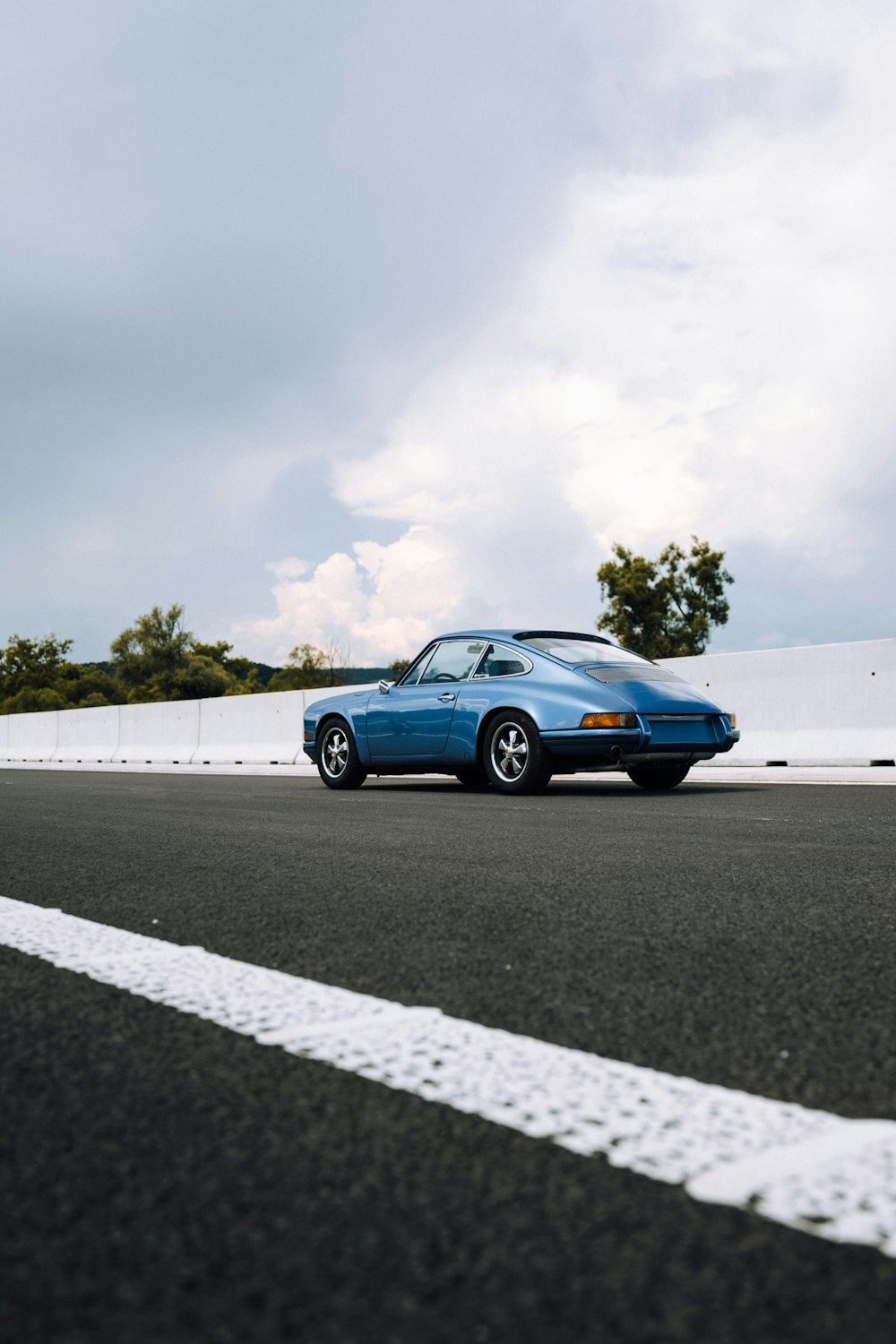 coupé blu sulla strada asfaltata grigia sotto il cielo nuvoloso bianco durante il giorno