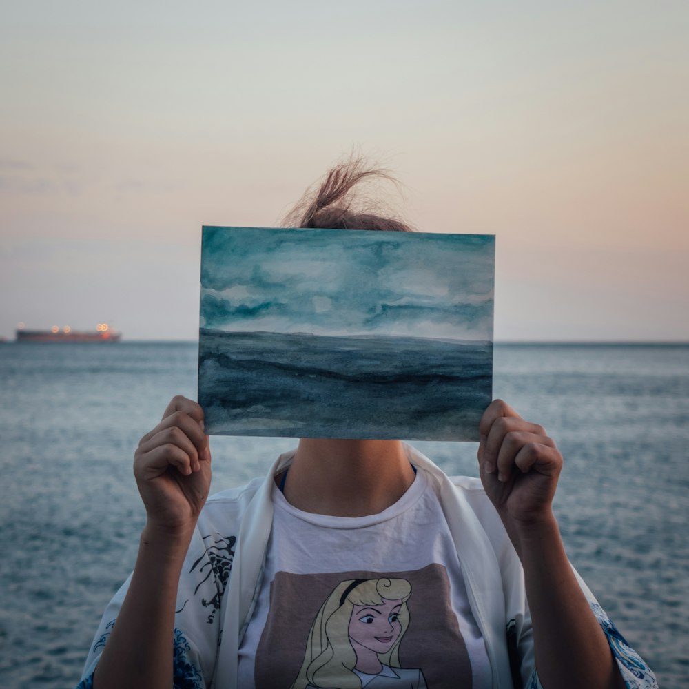 woman in white crew neck t-shirt holding blue and white painting