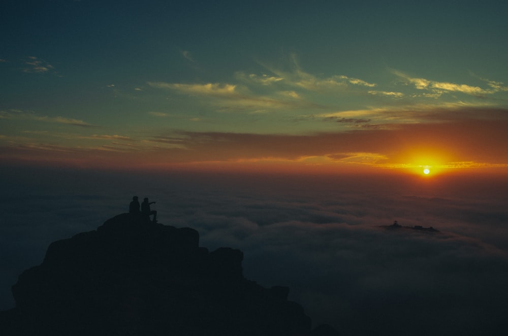 silhouette of people standing on rock formation during sunset