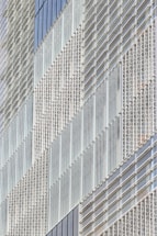 A modern building facade featuring a geometric pattern created by an array of glass panels and metal frames. The panels are arranged in a repetitive and structured manner, giving the structure a sleek and contemporary appearance.