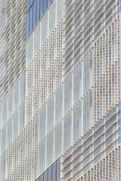 A modern building facade featuring a geometric pattern created by an array of glass panels and metal frames. The panels are arranged in a repetitive and structured manner, giving the structure a sleek and contemporary appearance.