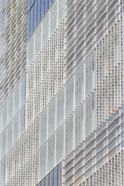 A modern building facade featuring a geometric pattern created by an array of glass panels and metal frames. The panels are arranged in a repetitive and structured manner, giving the structure a sleek and contemporary appearance.