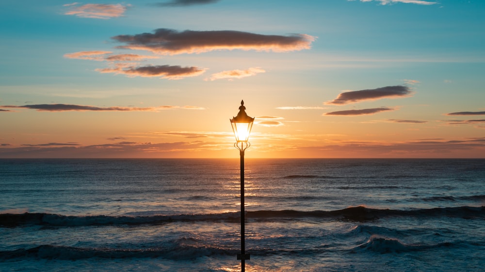 silhouette of lamp post on seashore during sunset