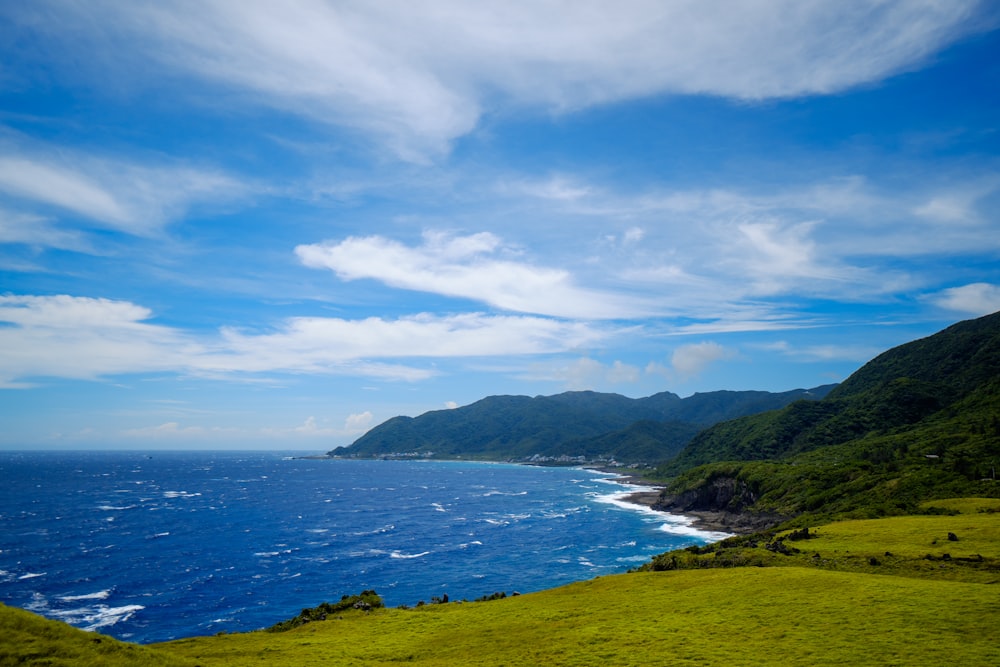 green grass field near body of water under blue sky during daytime