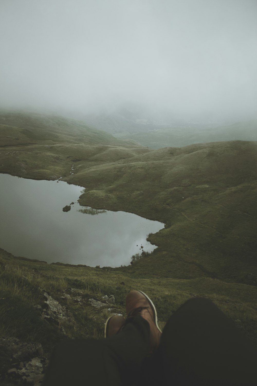 person in black pants sitting on green grass field near lake during daytime