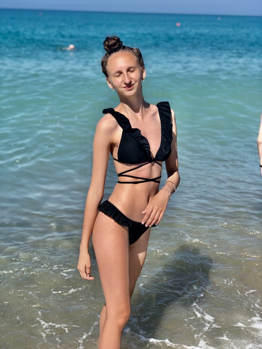 A smiling person wearing a coral adaptive bikini with side clips, standing confidently on a sunny beach.