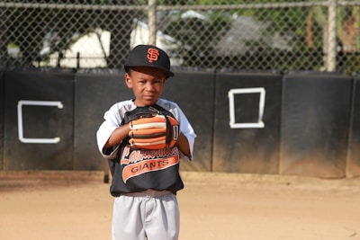 boy in orange and black jacket and white pants standing on field during daytime