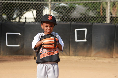 boy in orange and black jacket and white pants standing on field during daytime