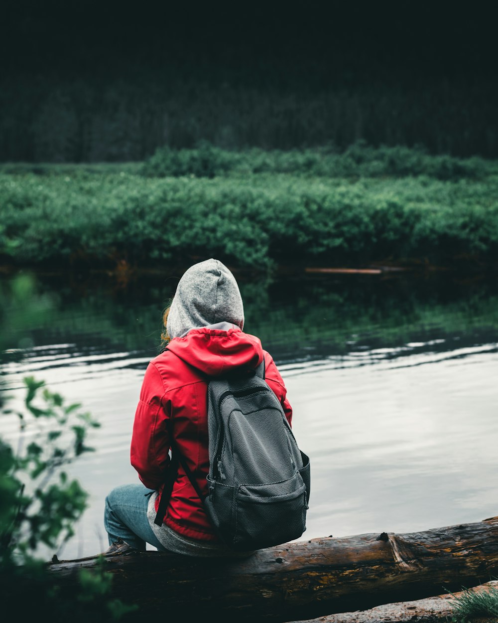 person in red and black hoodie sitting on wooden dock during daytime