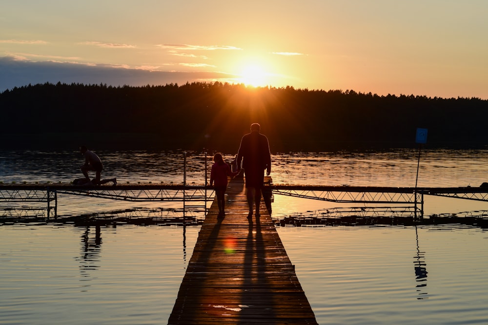 couple walking on wooden dock during sunset