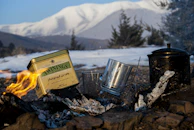 A Frostara thermos pouring hot tea into a cup beside a cozy campfire.