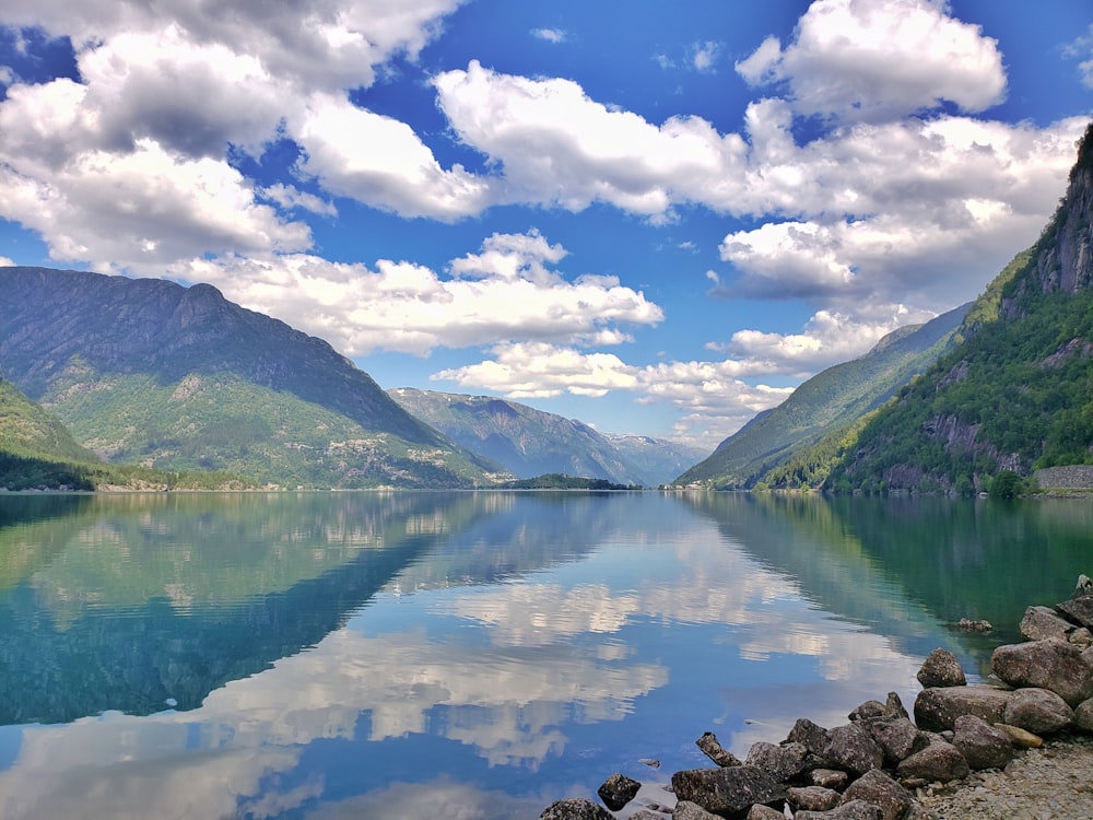 green mountains beside lake under blue sky and white clouds during daytime