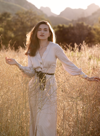 A model wearing a chic western dress with flowing fabric, standing against a sunlit garden backdrop.