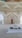 A beautifully decorated interior space blends classical Islamic architectural elements with modern design. Intricate geometric patterns adorn large windows, allowing light to filter through, casting intricate shadows on the floor. Ornate Arabic calligraphy decorates the walls, adding to the spiritual and cultural ambiance of the space. A small fountain or decorative water feature sits prominently in the center, enhancing the serene atmosphere.