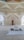 A beautifully decorated interior space blends classical Islamic architectural elements with modern design. Intricate geometric patterns adorn large windows, allowing light to filter through, casting intricate shadows on the floor. Ornate Arabic calligraphy decorates the walls, adding to the spiritual and cultural ambiance of the space. A small fountain or decorative water feature sits prominently in the center, enhancing the serene atmosphere.