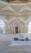 A beautifully decorated interior space blends classical Islamic architectural elements with modern design. Intricate geometric patterns adorn large windows, allowing light to filter through, casting intricate shadows on the floor. Ornate Arabic calligraphy decorates the walls, adding to the spiritual and cultural ambiance of the space. A small fountain or decorative water feature sits prominently in the center, enhancing the serene atmosphere.