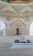 A beautifully decorated interior space blends classical Islamic architectural elements with modern design. Intricate geometric patterns adorn large windows, allowing light to filter through, casting intricate shadows on the floor. Ornate Arabic calligraphy decorates the walls, adding to the spiritual and cultural ambiance of the space. A small fountain or decorative water feature sits prominently in the center, enhancing the serene atmosphere.