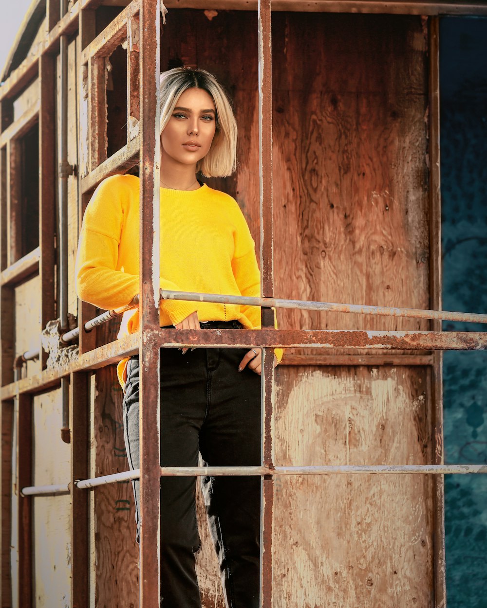 woman in yellow long sleeve shirt standing beside brown metal fence during daytime