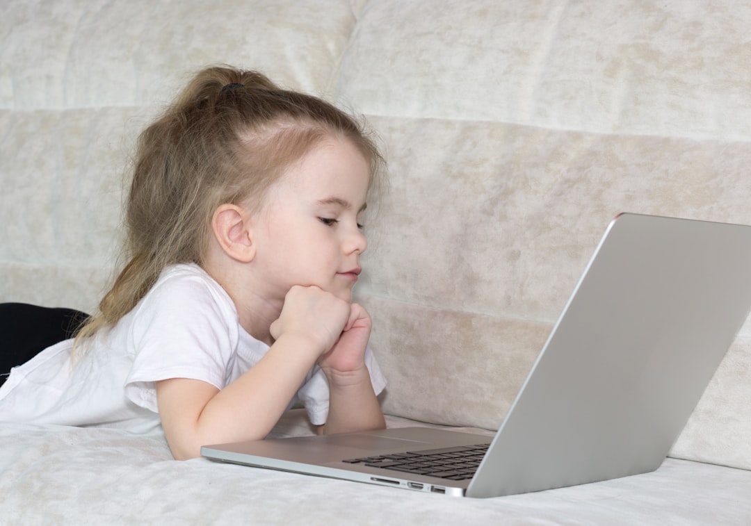 Little girl lying on bed in her room and watching cartoon on laptop.