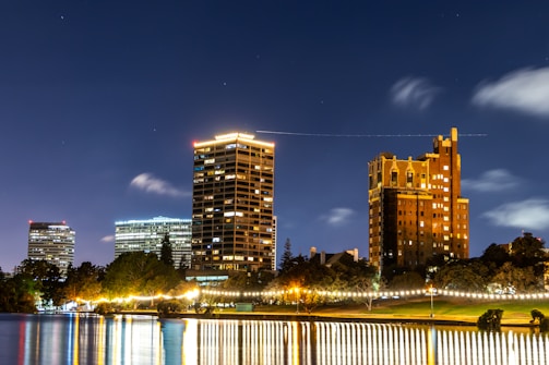 Evening skyline with illuminated buildings reflecting on calm water.