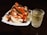 A white plate filled with pieces of jicama and mango, sprinkled with chili powder and tamarind candies on top. Beside the plate, there is a clear glass filled with a chilled beverage that appears to contain ice cubes.