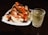 A white plate filled with pieces of jicama and mango, sprinkled with chili powder and tamarind candies on top. Beside the plate, there is a clear glass filled with a chilled beverage that appears to contain ice cubes.