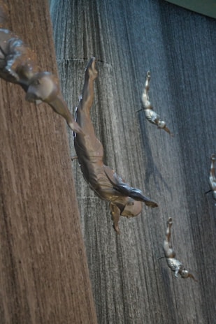 Several metallic sculptures of divers are attached to a large textured wall resembling a waterfall. The sculptures depict human figures in dynamic diving poses, creating the illusion of diving through water.