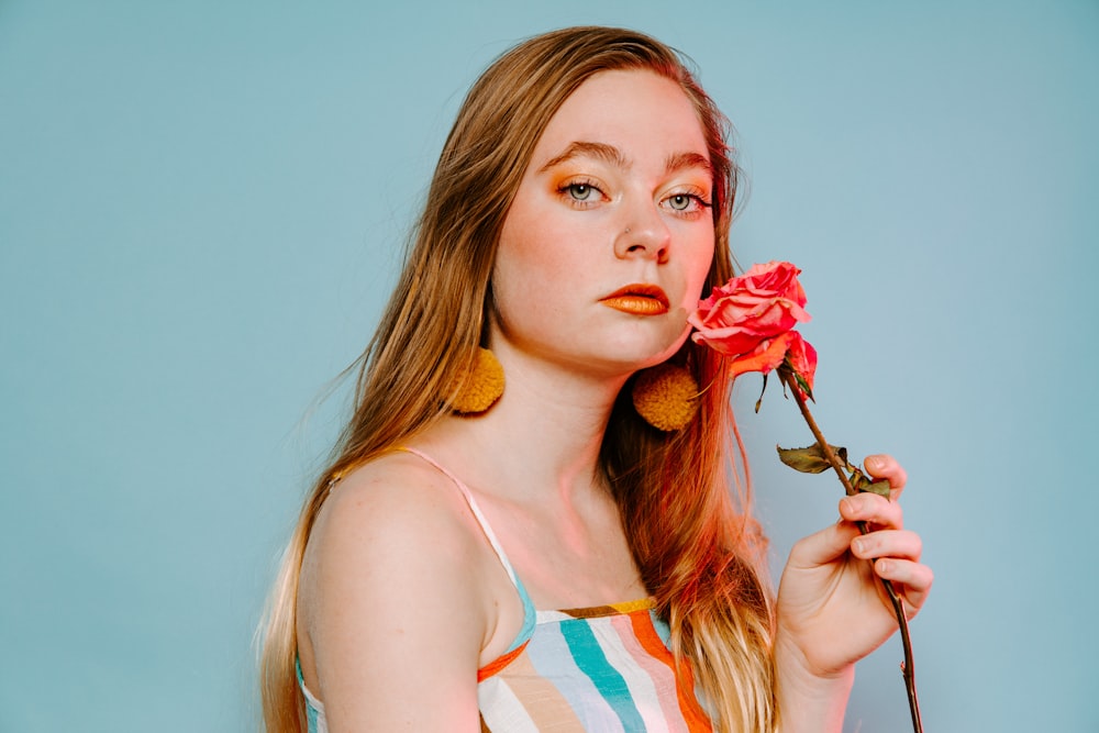 woman in white and orange tank top holding red flower