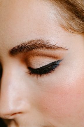 A close-up of a person's face focusing on the eye area, showcasing a perfectly shaped eyebrow and eye makeup with sleek black eyeliner and neutral eyeshadow.
