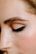A close-up of a person's face focusing on the eye area, showcasing a perfectly shaped eyebrow and eye makeup with sleek black eyeliner and neutral eyeshadow.
