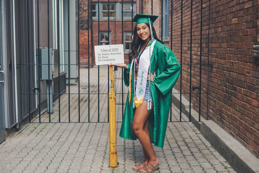 woman in green academic dress standing on sidewalk during daytime