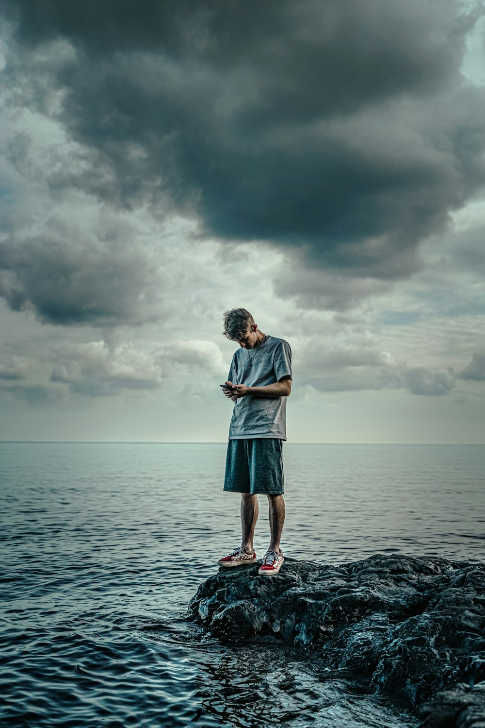 woman in white long sleeve shirt and blue skirt standing on rock in front of sea