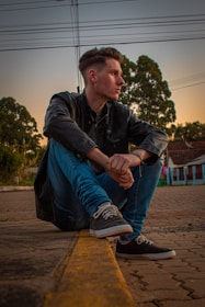 A man wearing a leather jacket, walking down a city street at sunset.